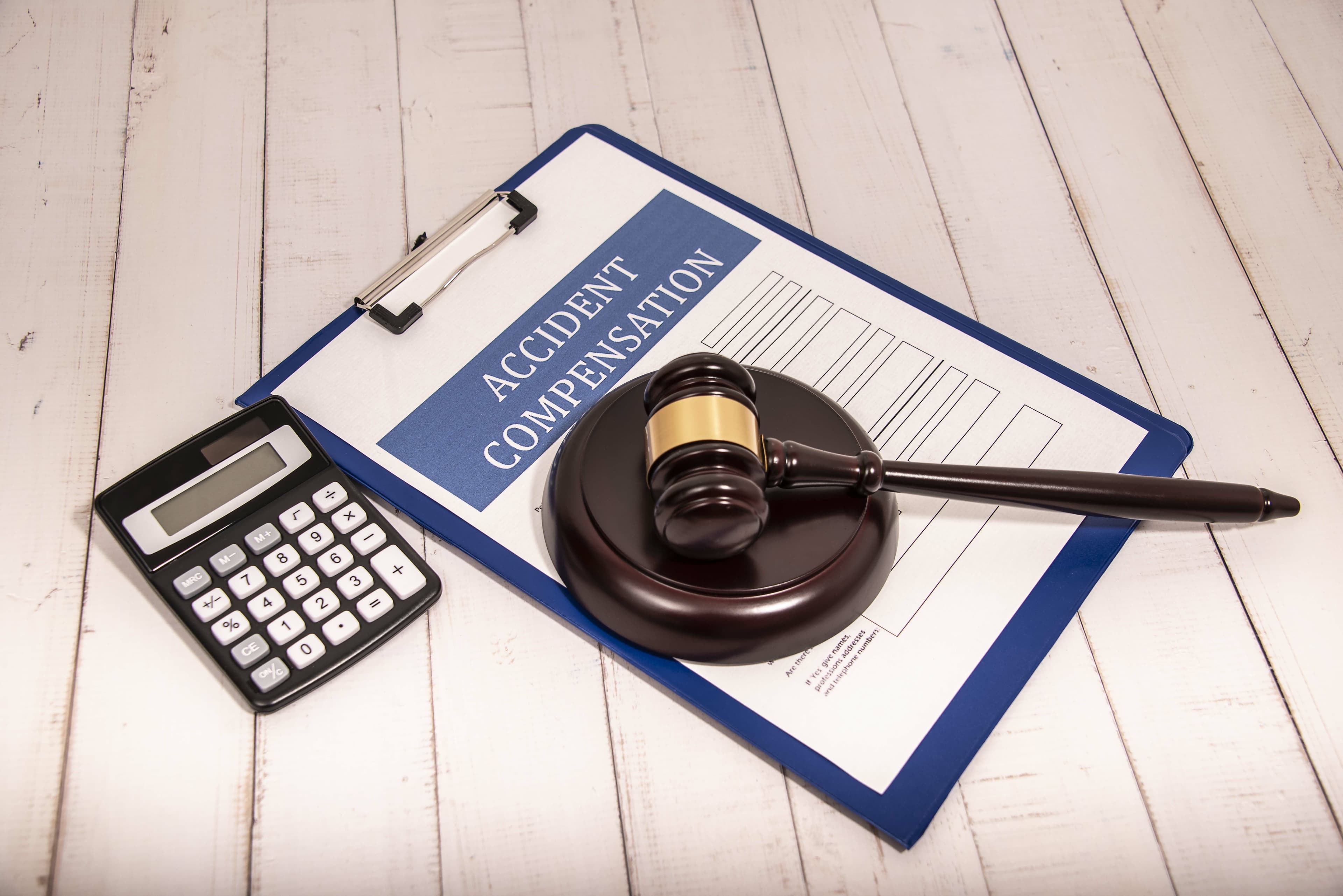 Dark wooden gavel laying on top of an accident report. Black calculator laying next to accident report. | Personal Injury | The Sullivan Law Firm